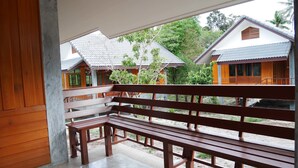 A wooden bench in a covered outdoor area with a view of traditional-style buildings and greenery. - Nature Home (Ko Pha-ngan)