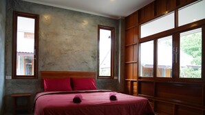 A bedroom with a wooden bed, two windows, a small bedside table, and a concrete floor. - Nature Home (Ko Pha-ngan)