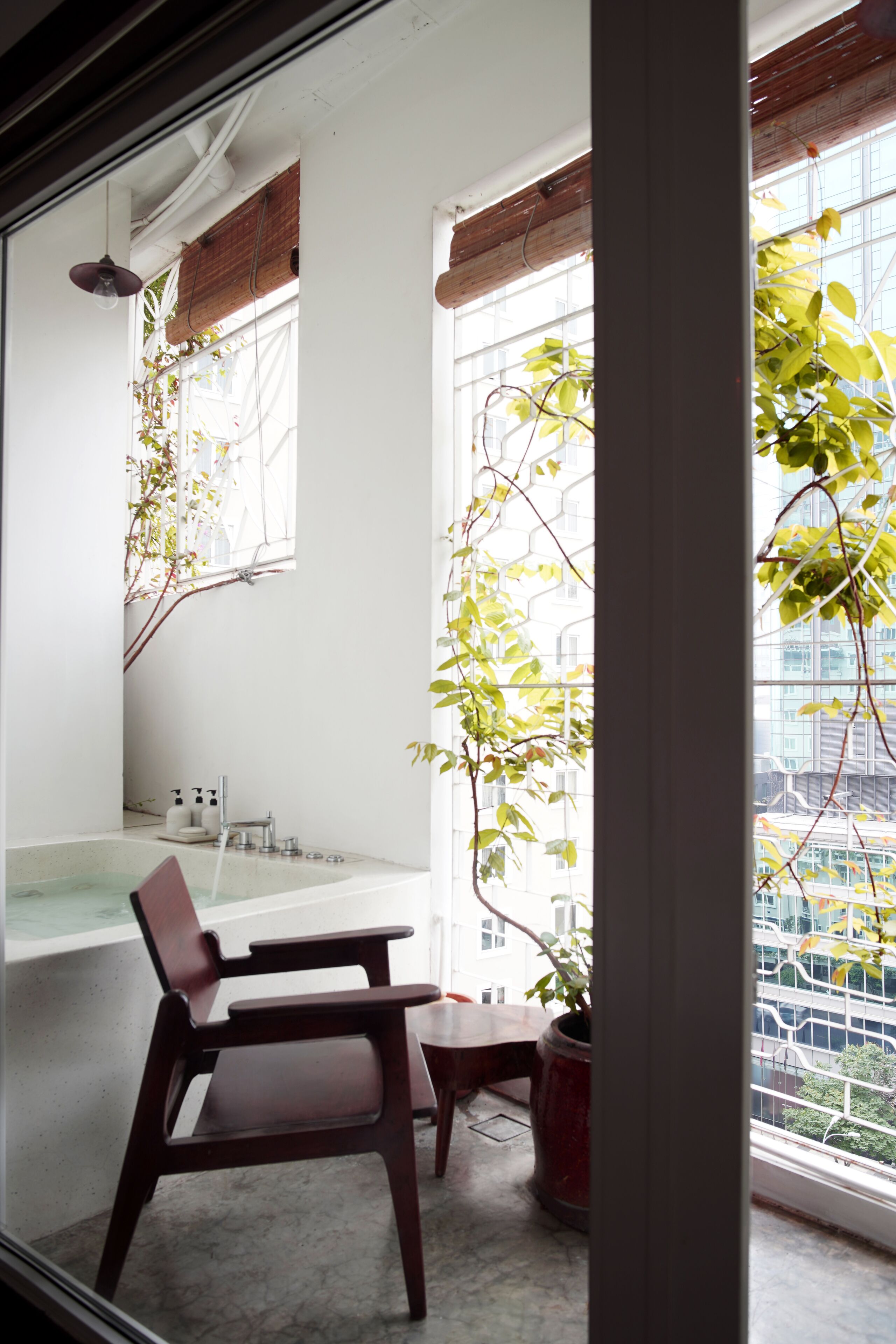 Une salle de bain avec une baignoire, un lavabo et un miroir. Il y a une fenêtre qui donne sur les bâtiments à l’extérieur.