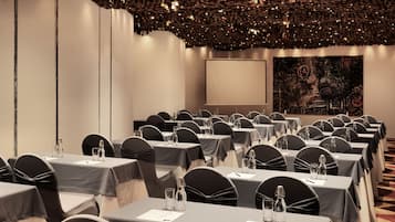 Ein Konferenzraum mit Reihen von Tischen, schwarzen Stühlen und einer Projektionsleinwand.