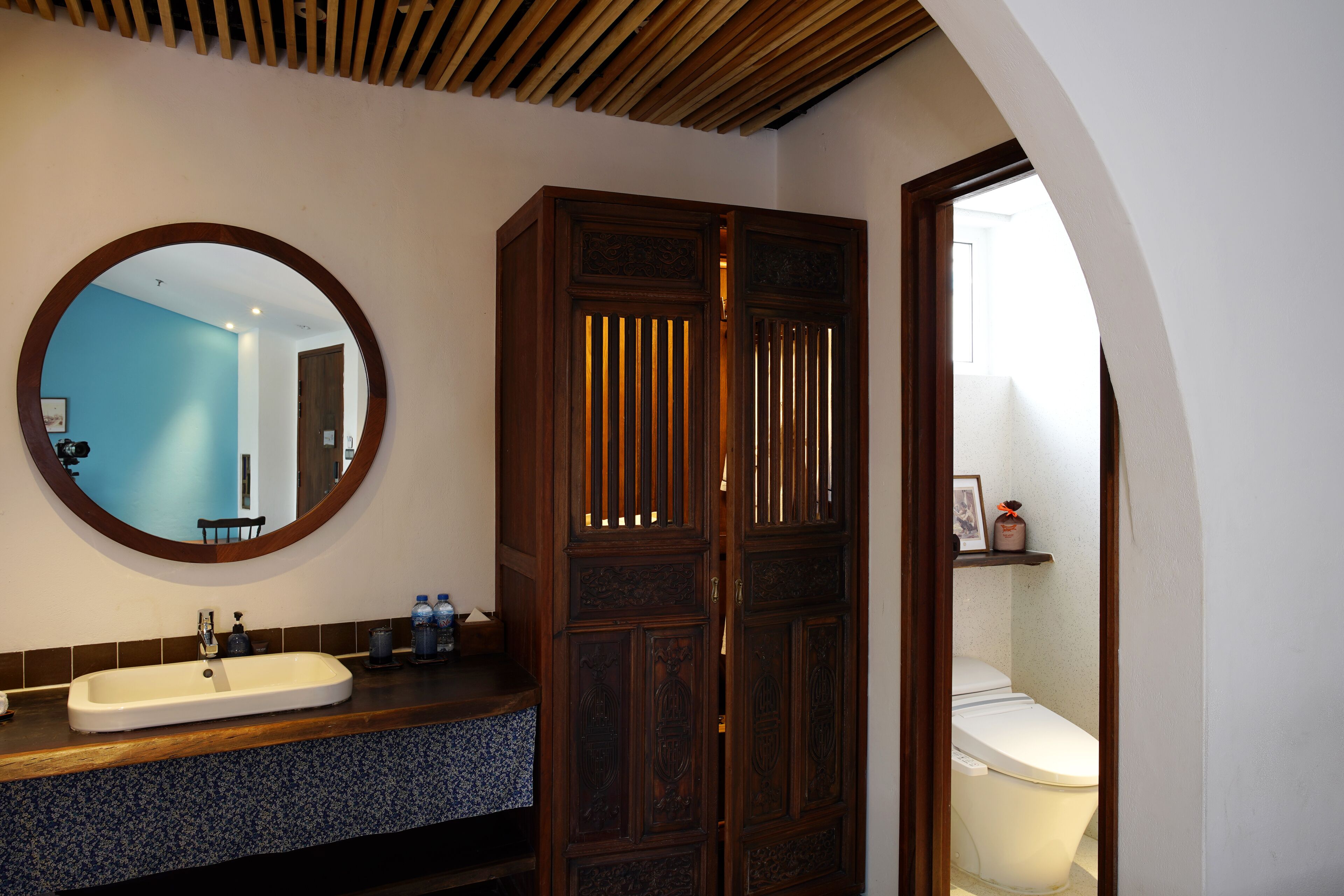 A bathroom with a wooden cabinet, a round mirror, and a toilet.
