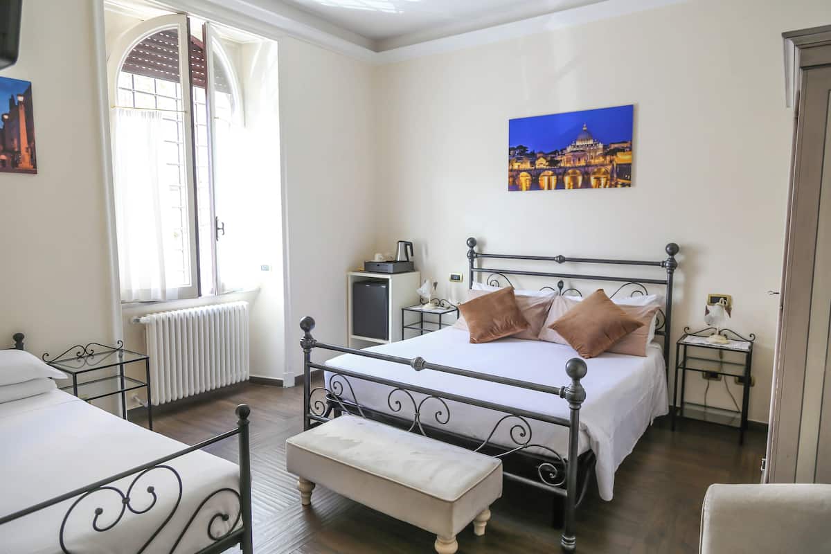 A bedroom with a bed, a bench, a nightstand, a radiator, a window, and a painting on the wall.