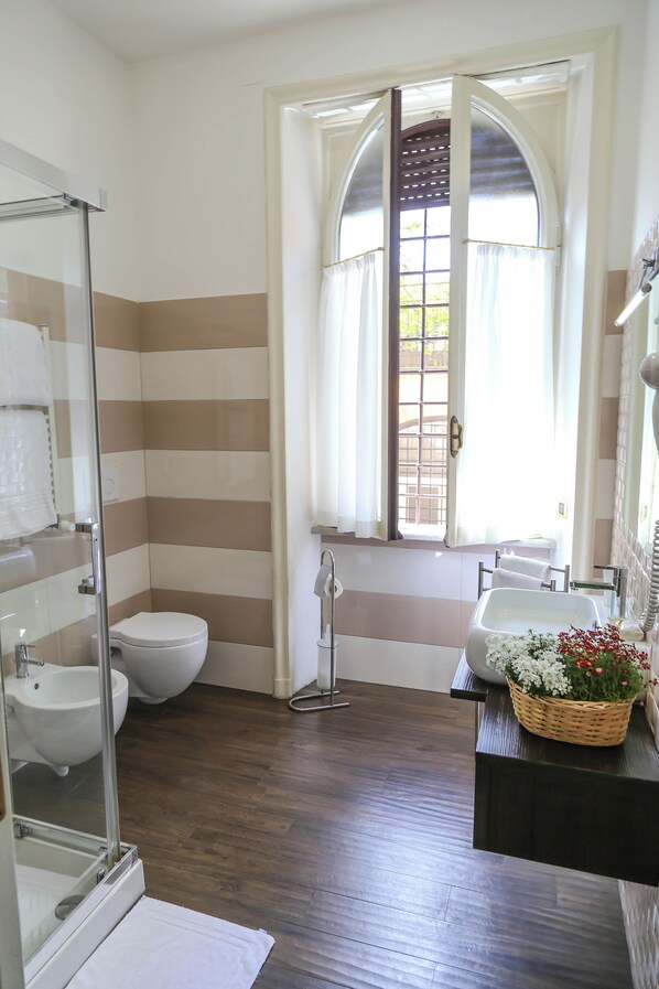 Un baño con cabina de ducha de vidrio, inodoro blanco, bidé y lavamanos con una cesta decorativa.