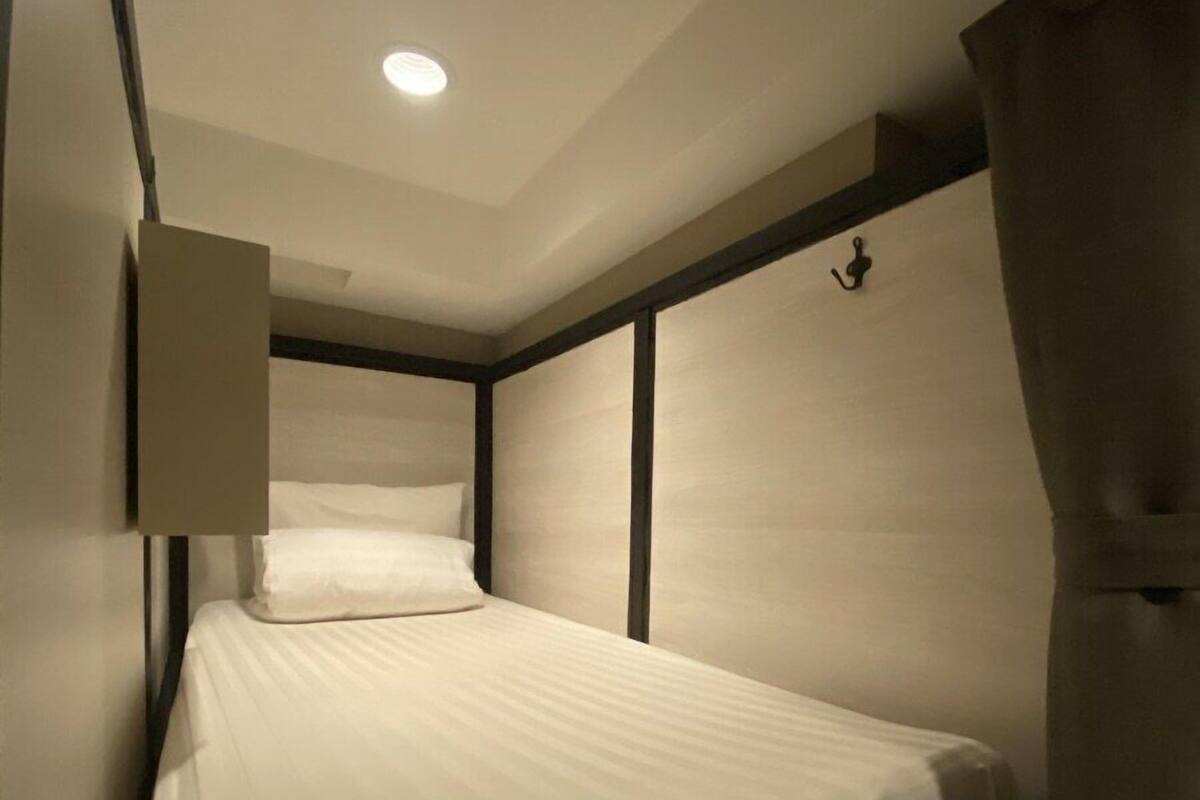 A single bed with a white mattress and headboard, a bedside table, and a wall-mounted light fixture.