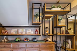 A room with wooden furniture, a desk with a mirror, shelves with decorative items, and a wall-mounted shelf with plants.