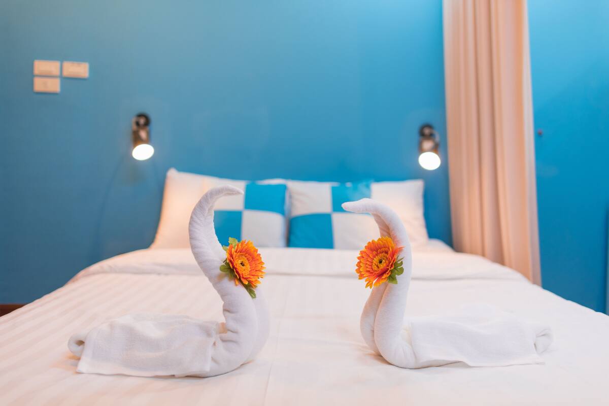A bed with white bedding and two swan-shaped towels with orange flowers.