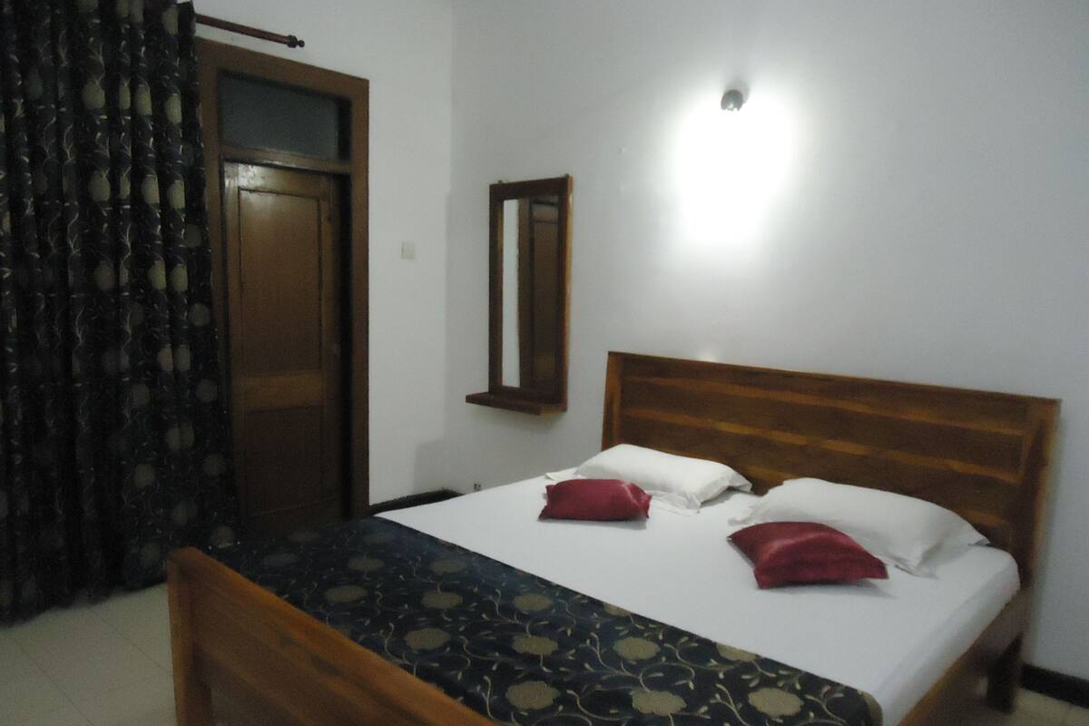 A bedroom with a wooden bed, a mirror, and a curtain.