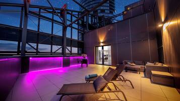 A rooftop lounge with sun loungers, a table, and a view of the night sky.