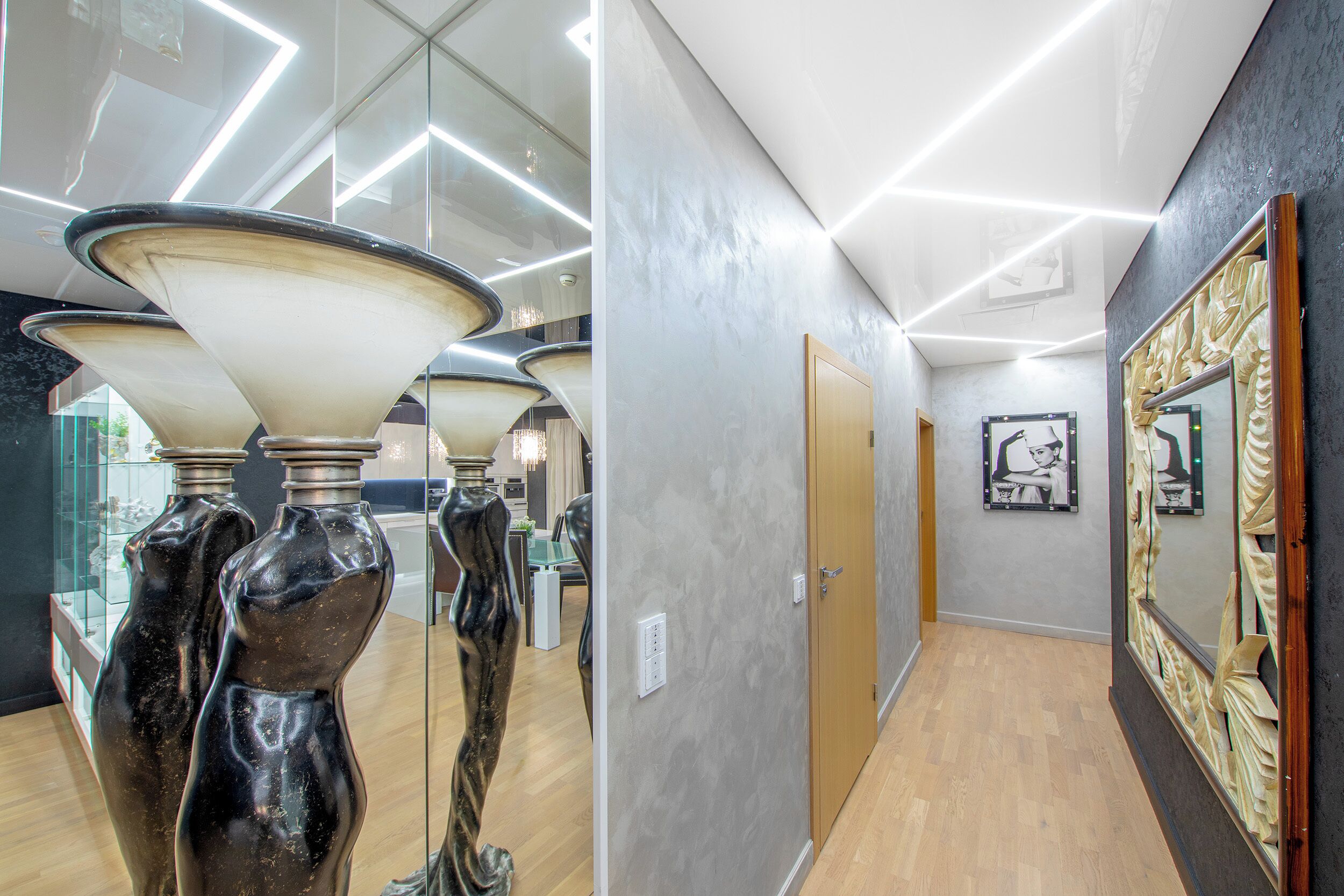 Een modern interieur met een hal, een houten vloer en een glazen vitrine met decoratieve objecten.