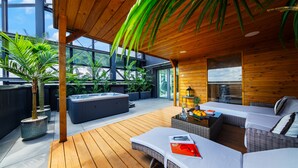 A modern outdoor living area with a wooden deck, a hot tub, and a seating area with a sofa and a table. - Sky Tower Apartments (Wroclaw)