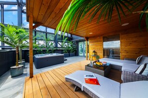 A modern outdoor living area with a wooden deck, a hot tub, and a seating area with a sofa and a table. - Sky Tower Apartments (Wroclaw)