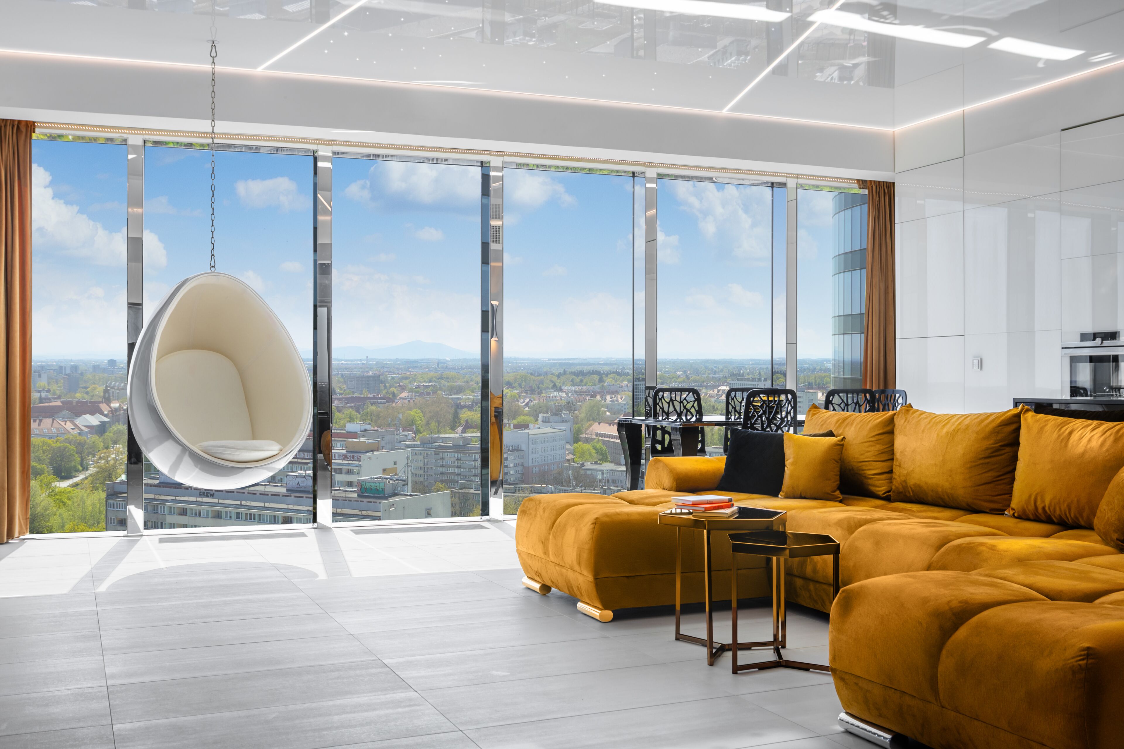 A modern living room with a large window, a hanging chair, a sofa, and a small table.