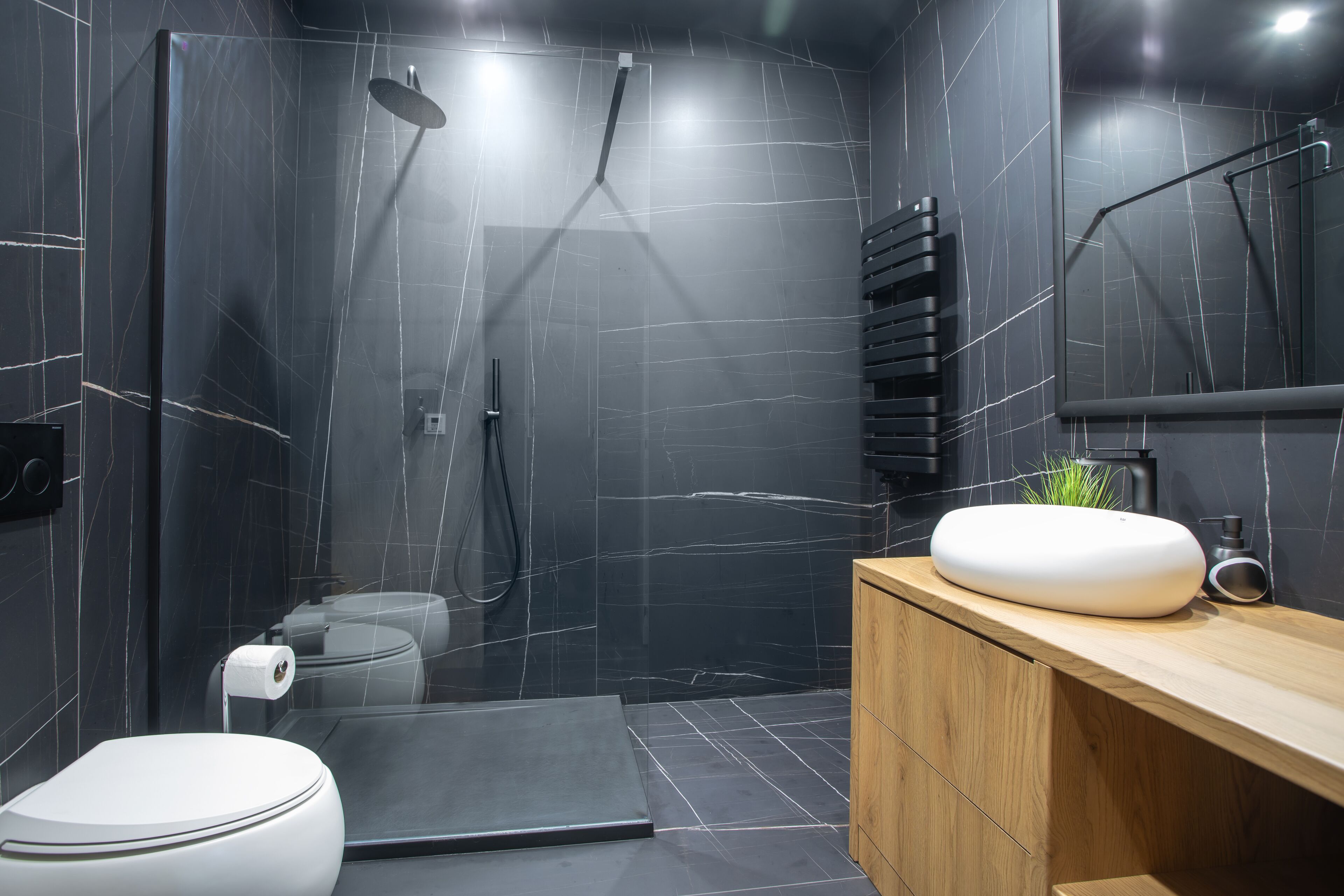 A modern bathroom with a black marble wall, a wooden vanity, a white toilet, and a shower area.
