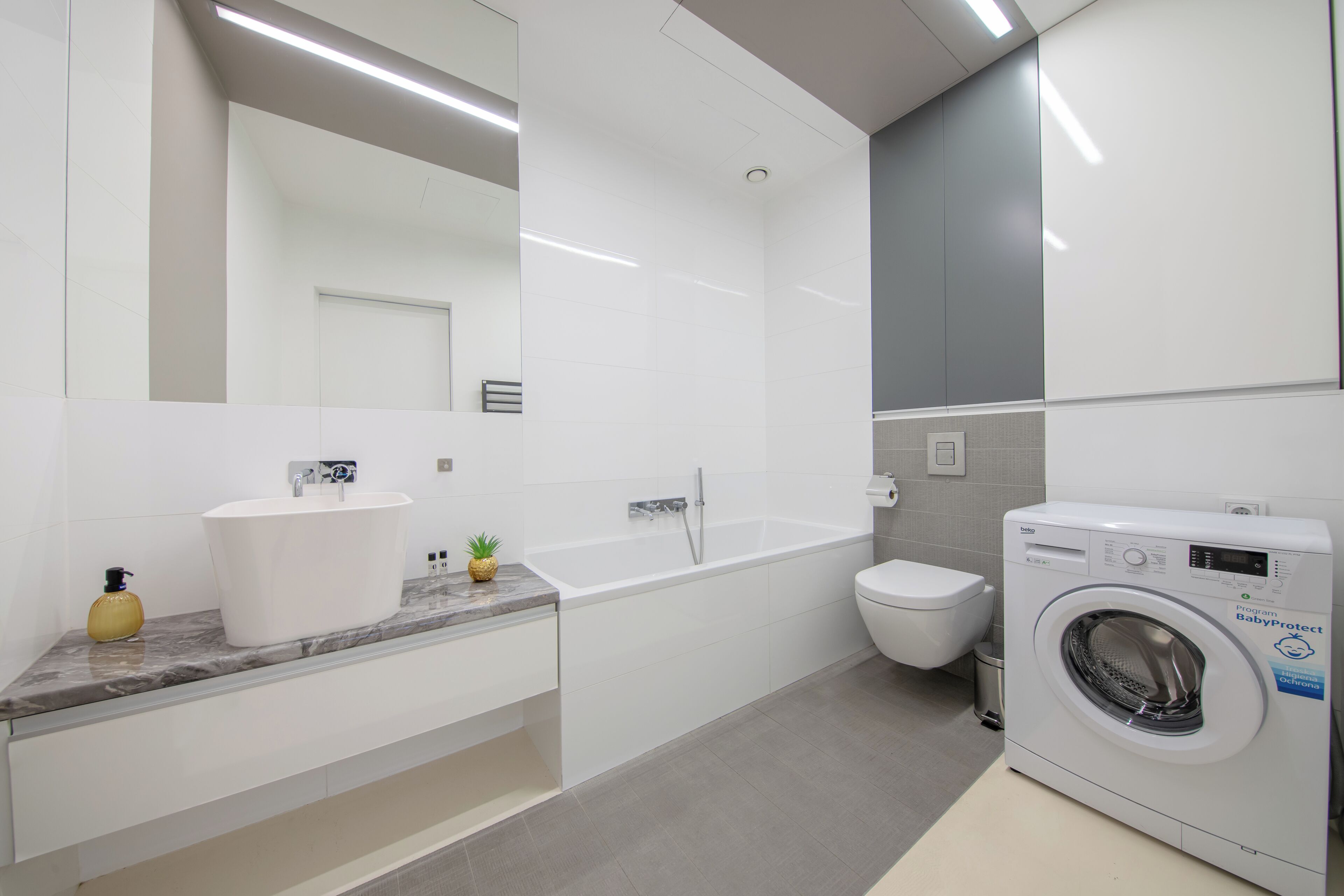 A modern bathroom with a white sink, a bathtub, a toilet, and a front-loading washing machine.