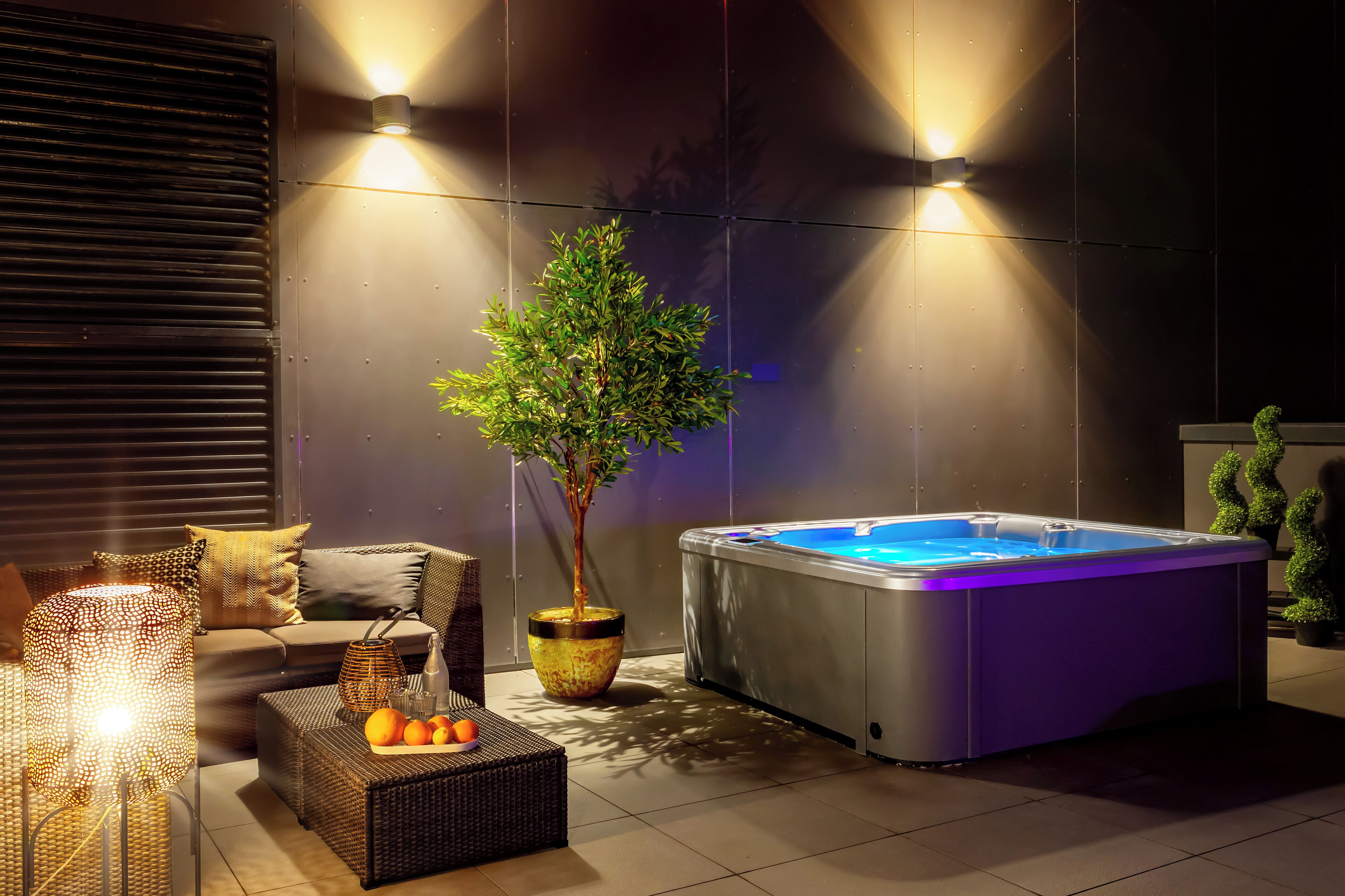 A modern outdoor area with a hot tub, wicker furniture, and ambient lighting.