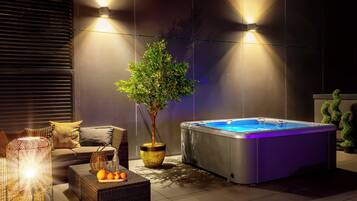 A modern outdoor area with a hot tub, wicker furniture, and ambient lighting.