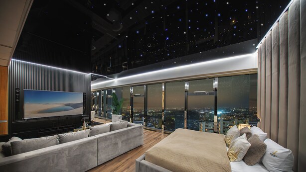 A modern hotel room with a city view, a large flat-screen TV, a sofa, and a bed. - Sky Tower Apartments (Wroclaw)
