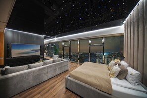 A modern hotel room with a city view, a large flat-screen TV, a sofa, and a bed. - Sky Tower Apartments (Wroclaw)