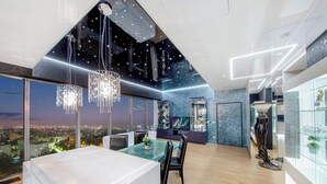 A modern kitchen with a large island, a dining area with chairs, and a view of the city at night. - Sky Tower Apartments (Wroclaw)