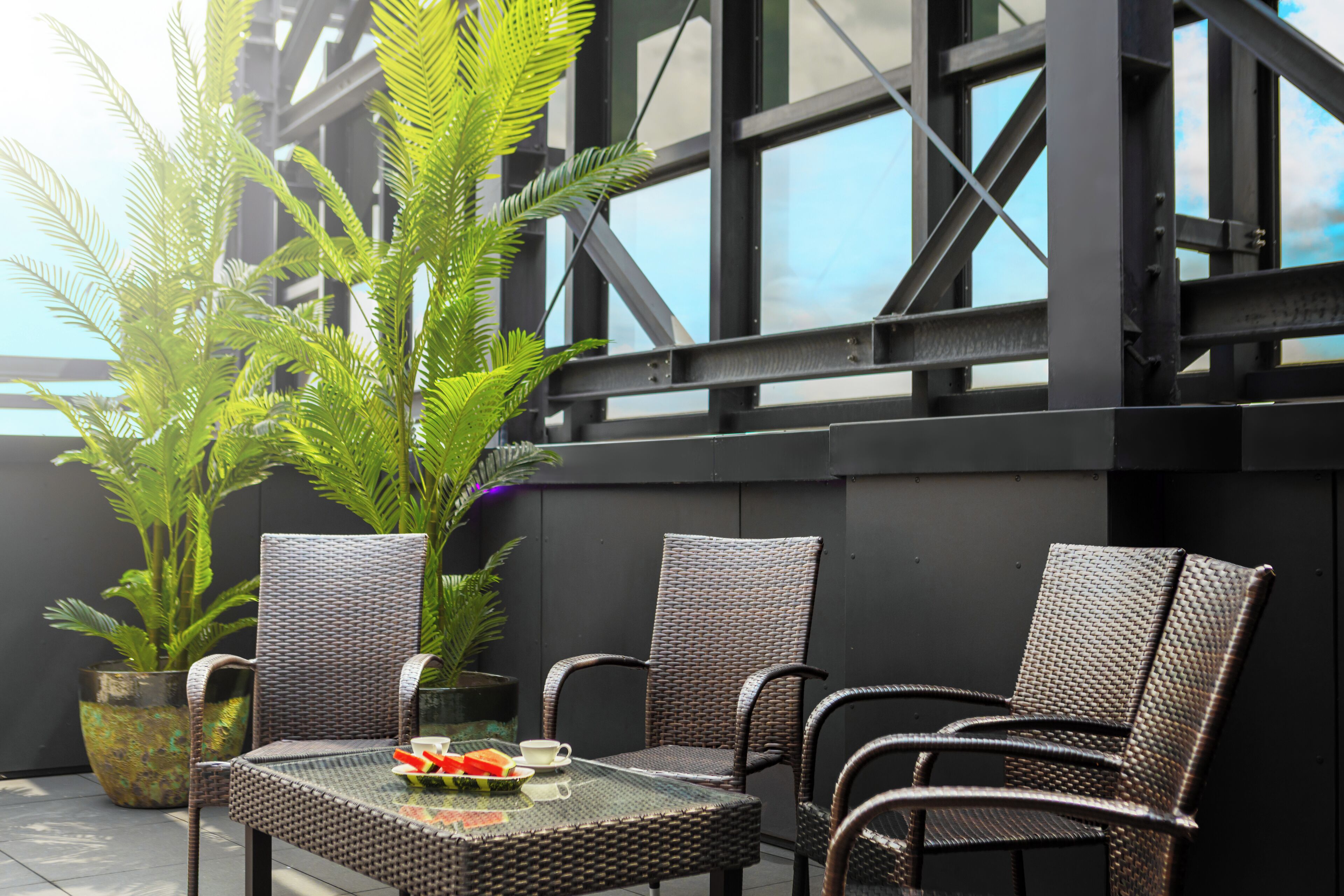 A balcony with wicker furniture, a glass table, and a potted plant.