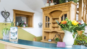 A reception area with a wooden cabinet, a blue counter, and a white vase with flowers. - Arracher Hof (Arrach)