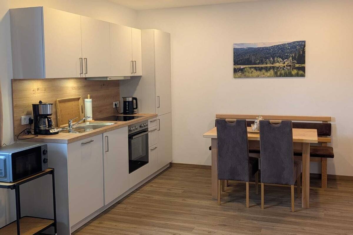 A compact kitchen with white cabinets, a wooden countertop, a coffee maker, a microwave, and a dining area with a table and chairs.