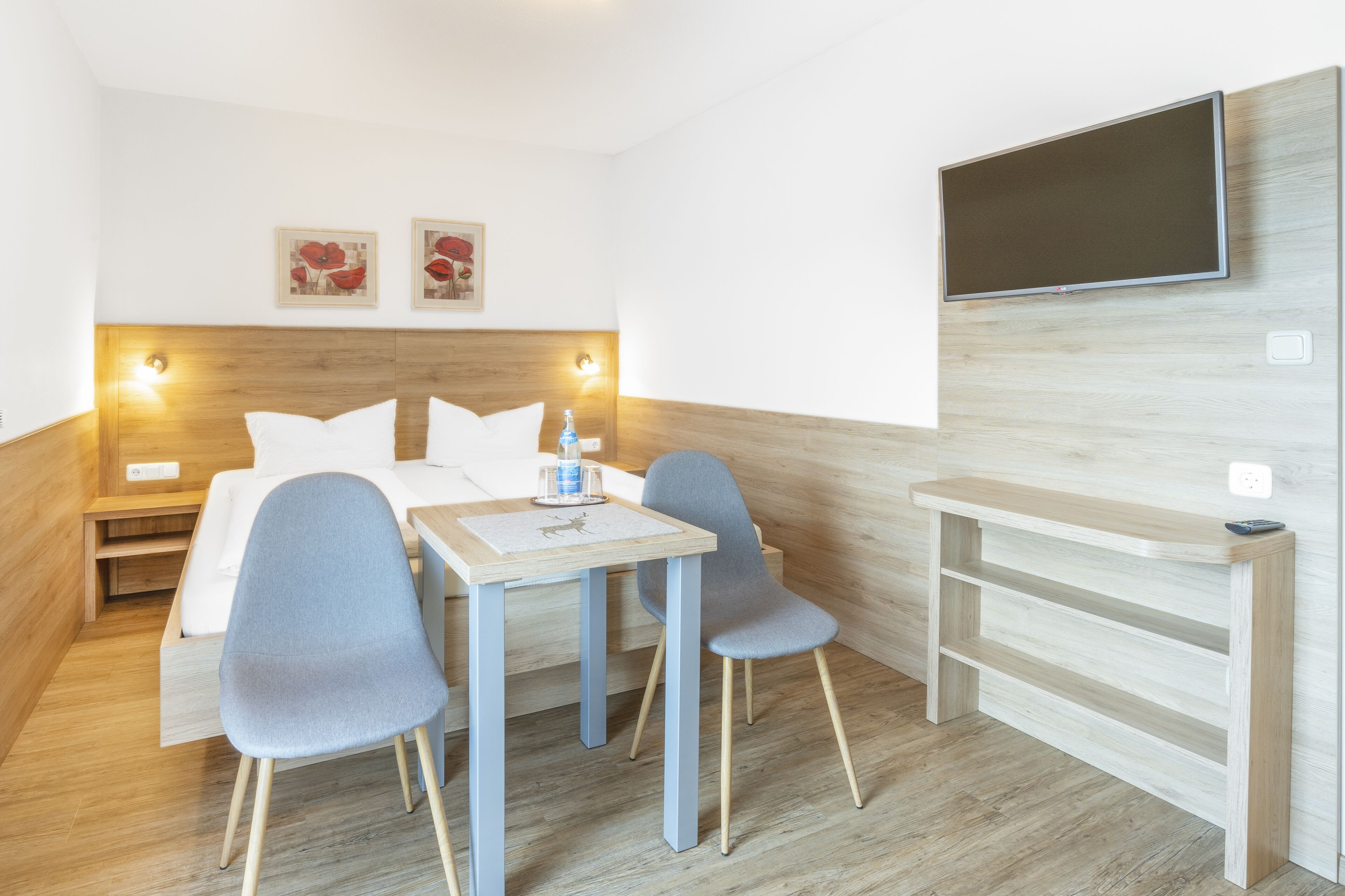 A hotel room with a bed, a desk, two chairs, a TV, and artwork on the wall.