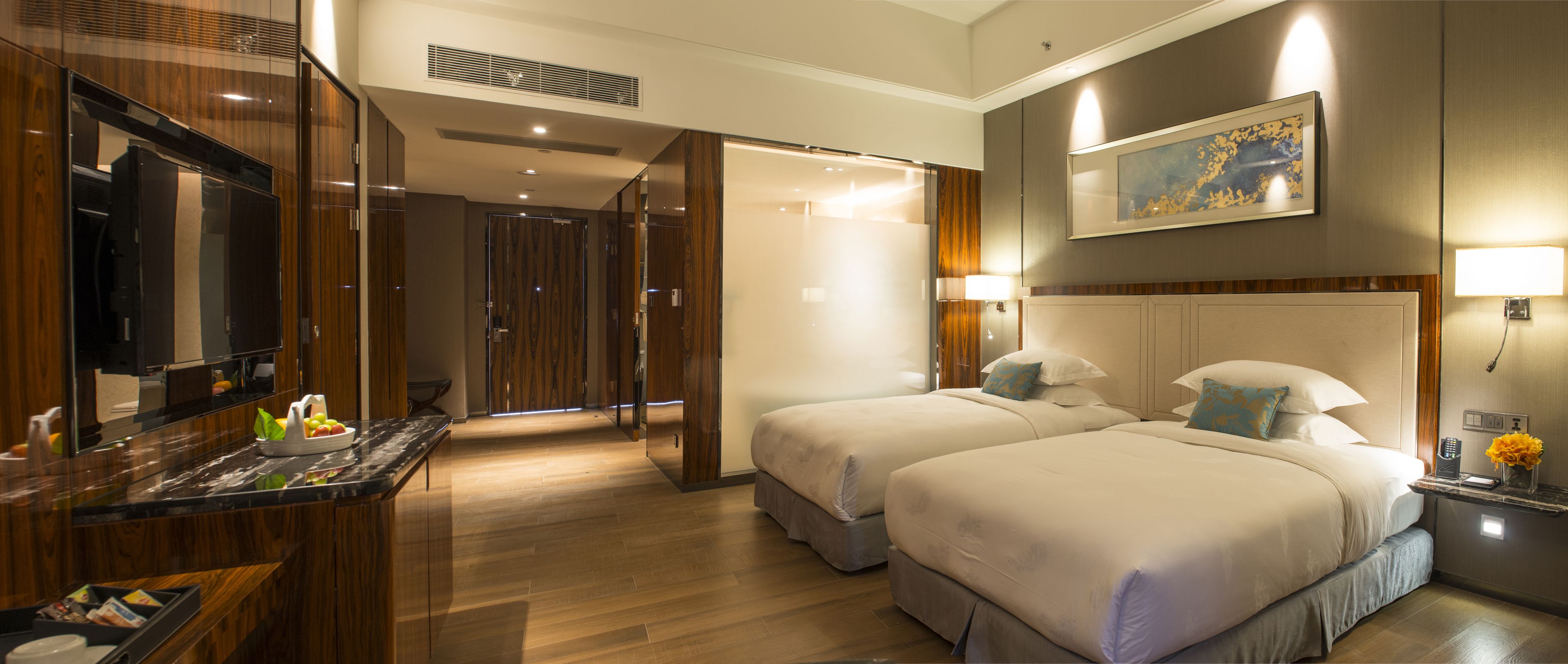 A hotel room with two beds, a bathroom, a desk with a mirror, and a painting on the wall.