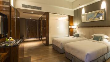 A hotel room with two beds, a bathroom, a desk with a mirror, and a painting on the wall.