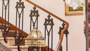 A staircase with ornate metal railings and a wooden handrail, leading to a landing area with a desk and a vase of flowers. - Hotel Stefania (Cesenatico)