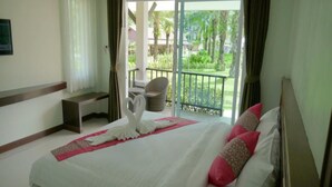 Habitación de hotel con cama, un banco, una silla y un balcón con vistas a zonas verdes.