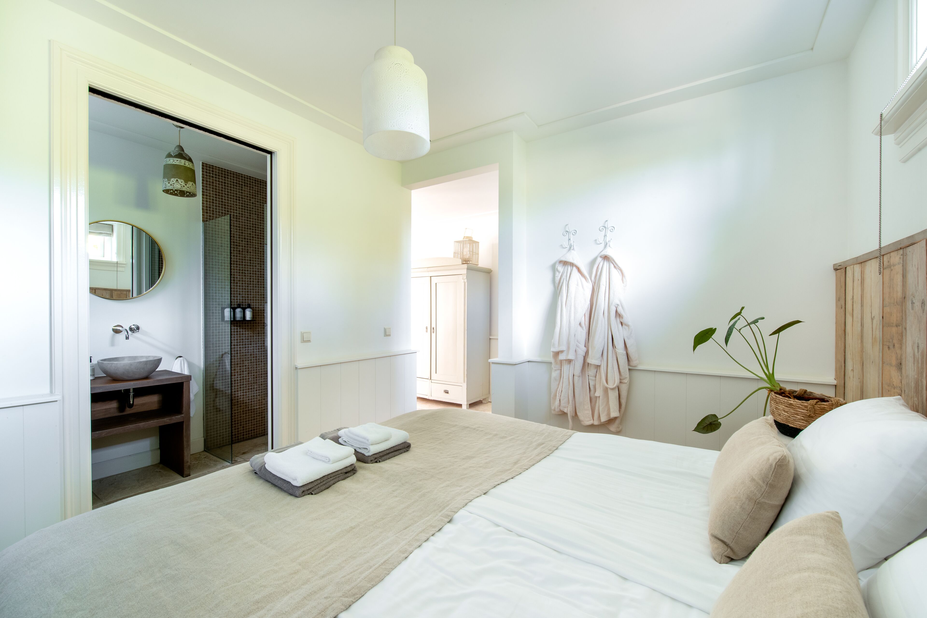 A modern bedroom with a large bed, a wooden vanity, a round mirror, and a walk-in closet.