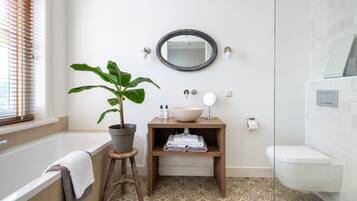Een badkamer met een bad, een wastafel met spiegel, een potplant en een toilet.