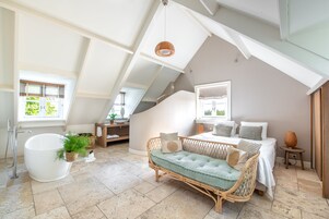 Um quarto amplo no estilo loft, com uma grande janela, uma banheira embutida, um sofá de rattan aconchegante e uma cama bem arrumada.