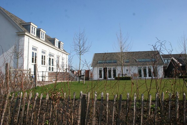 A residential area with two houses, one with a white facade and the other with a brown roof, surrounded by a wooden fence and bare trees. - Villa Oldenhoff (Abcoude)