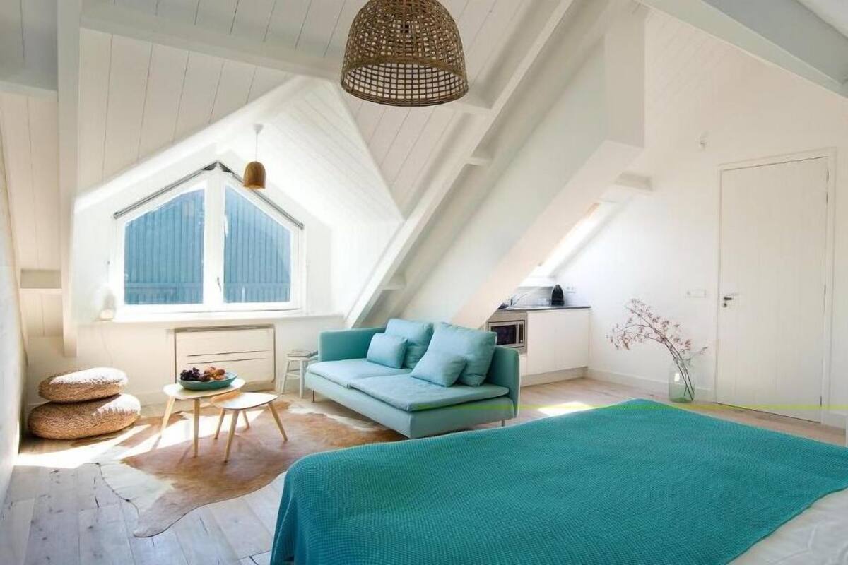 A spacious attic bedroom with a large window, a teal sofa, and a bed with a teal blanket.