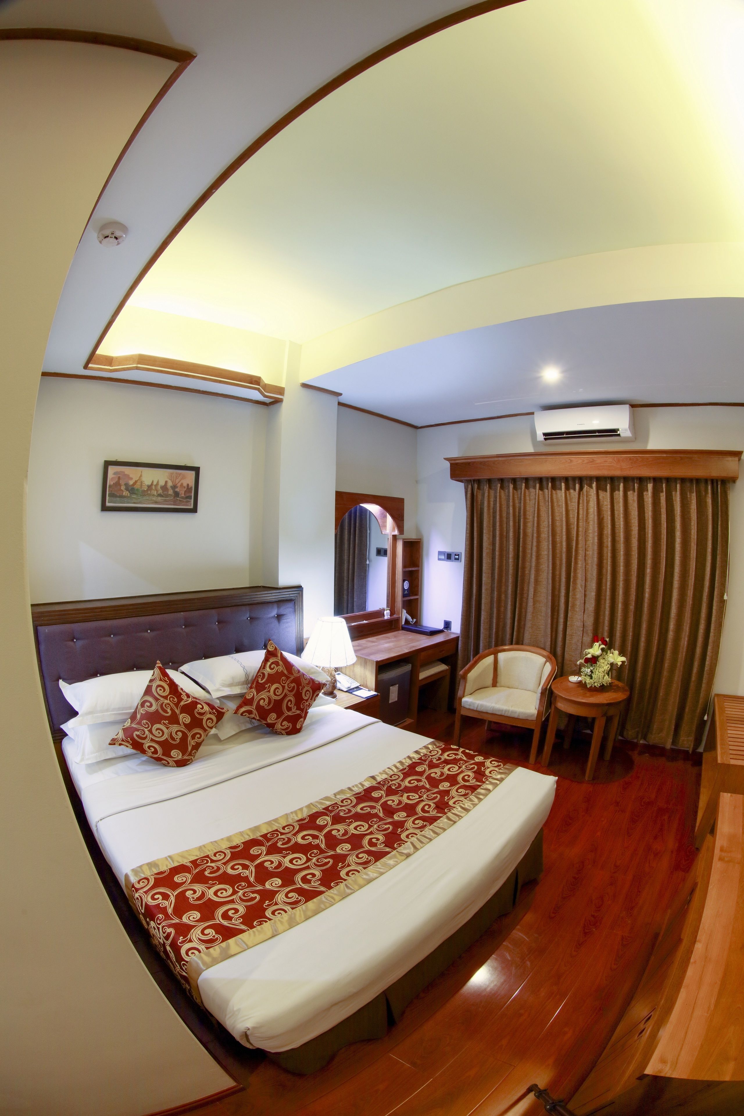A hotel room with a large bed, a desk, a chair, and a small table with a vase.
