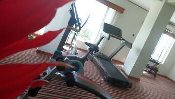 Un gimnasio con equipo de ejercicio, alfombra estampada y ventanas amplias.