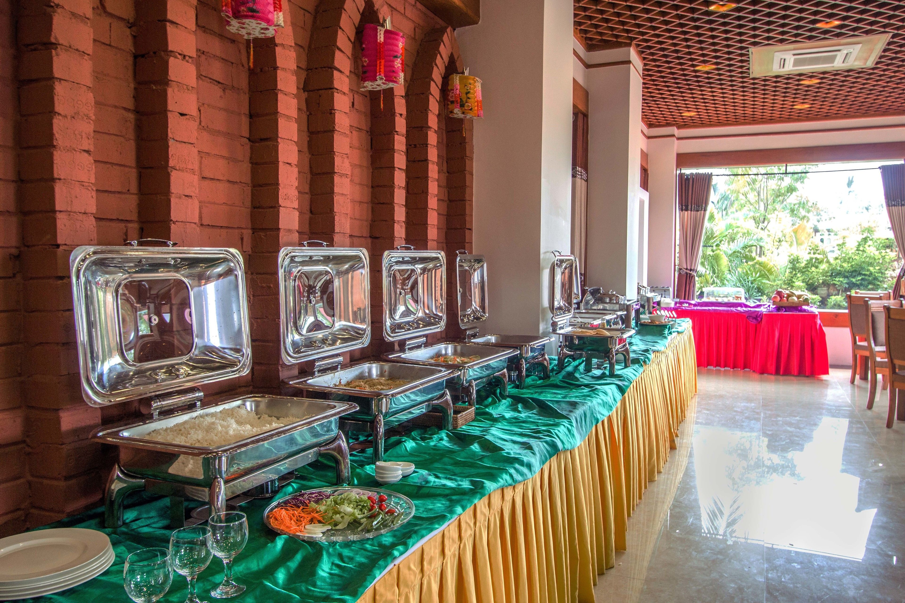 A buffet setup with multiple food service stations, a green tablecloth, and a brick wall backdrop.
