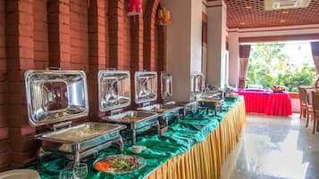 A buffet setup with multiple food service stations, a green tablecloth, and a brick wall backdrop.
