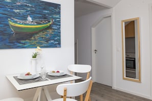 Uma área de refeições com uma mesa posta para dois, um quadro de um barco na água e vista para uma cozinha com forno.