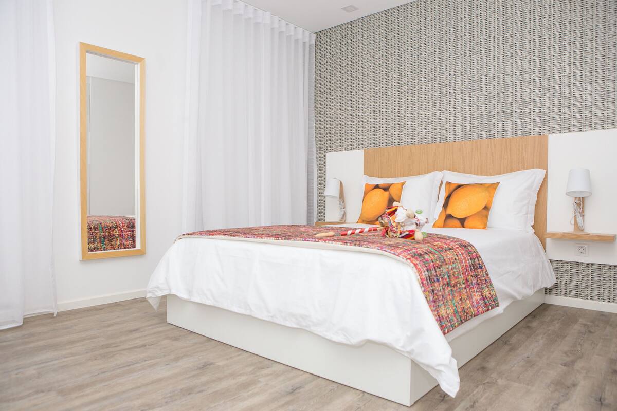 Une chambre moderne avec un grand lit, un miroir et un mur décoré d’un motif.