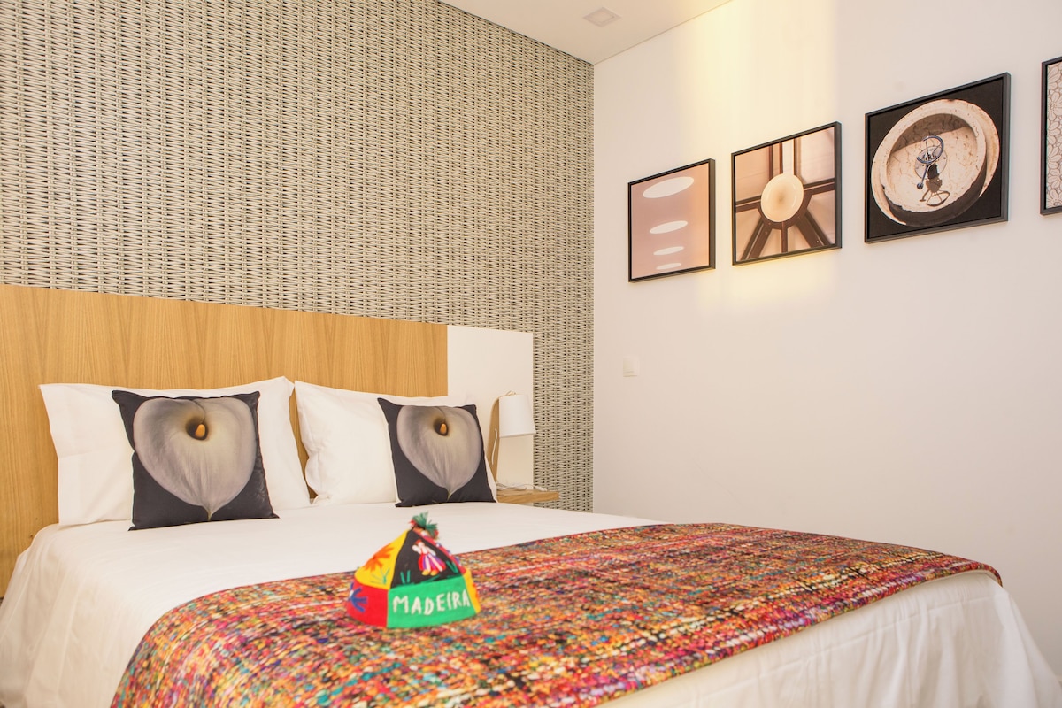 Una habitación de hotel con una cama, un colorido mantón tejido y una pared con textura.