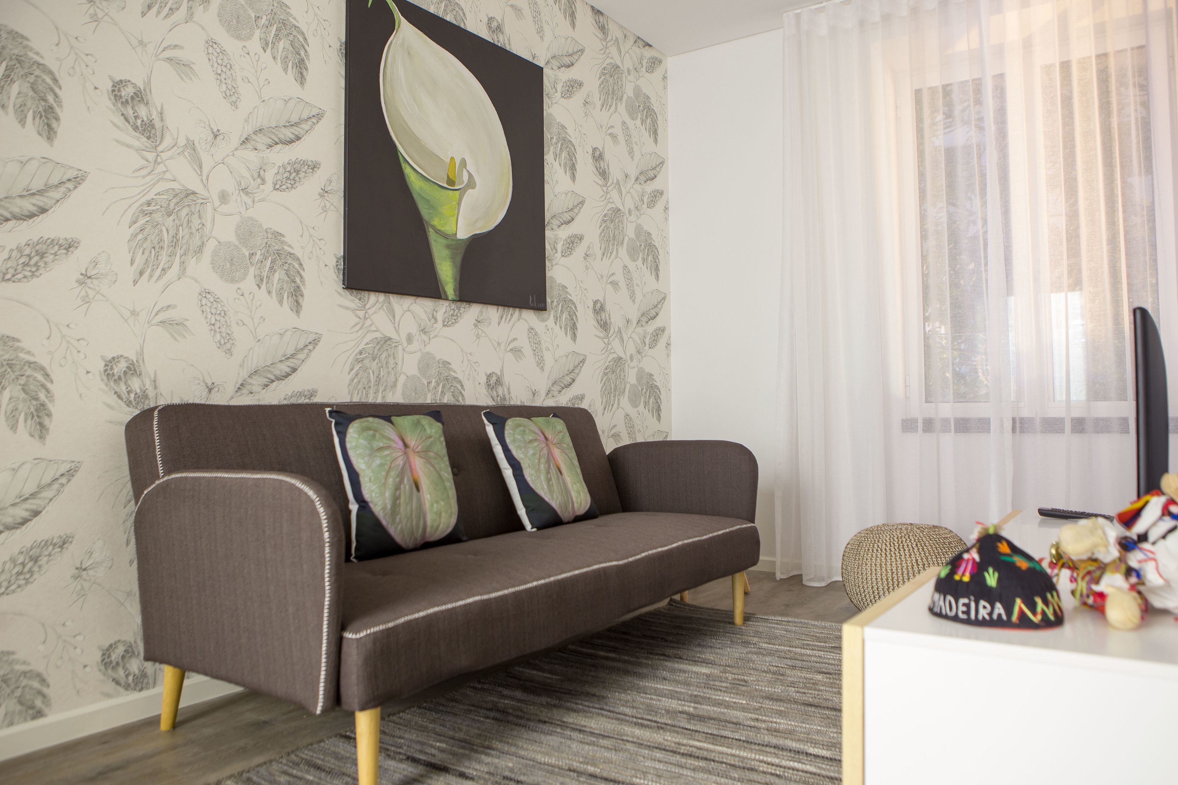 A living room with a sofa, a patterned wallpaper, a painting, and a window with curtains.