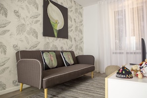 Sala de estar com sofá, papel de parede estampado, um quadro e janela com cortinas.