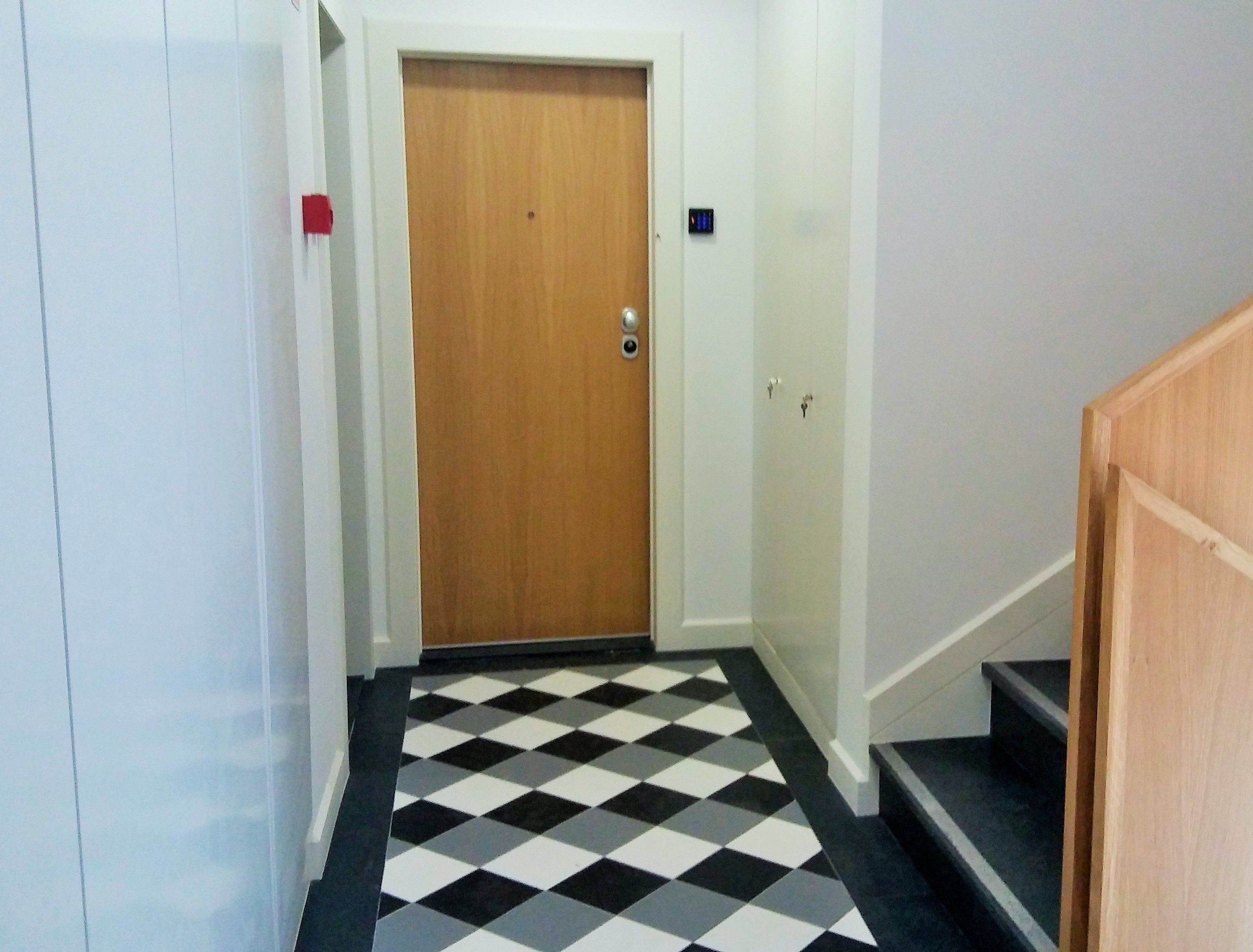 Un couloir avec un sol à carreaux, une porte en bois et un escalier.