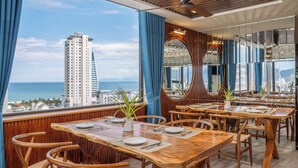 Een restaurant met houten tafels en stoelen, een grote spiegel en uitzicht op de oceaan en een hoog gebouw.