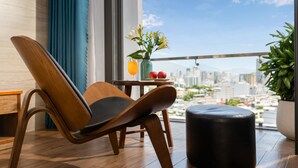 Een moderne kamer met een houten stoel, een tafeltje met een bloevas en uitzicht op de stad.