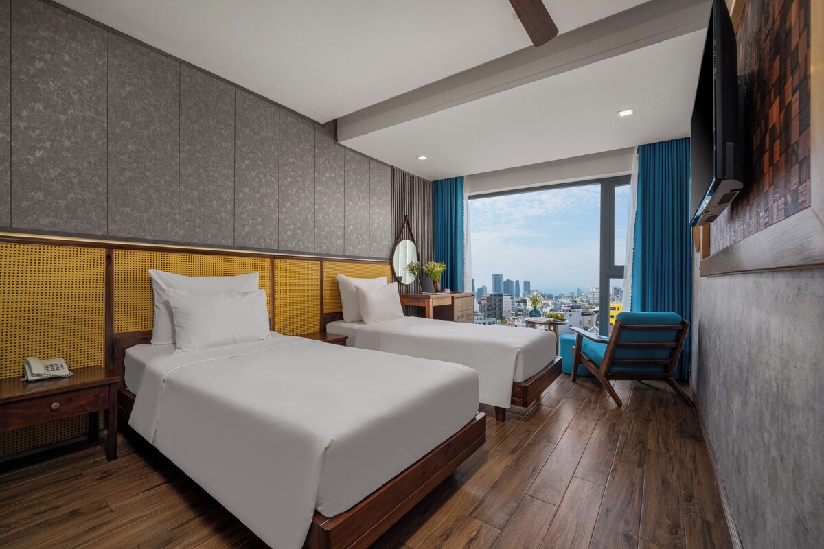 A hotel room with two beds, a desk, a chair, a TV, and a city view.
