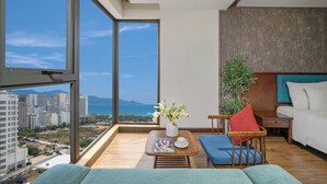 Ein modernes Zimmer mit großem Fenster, Holzboden, blauem Sofa, kleinem Tisch mit Vase und weißem Bett.